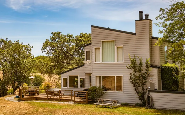 Two-story home with neutral siding, white window trim, and a wood deck beside a lawn