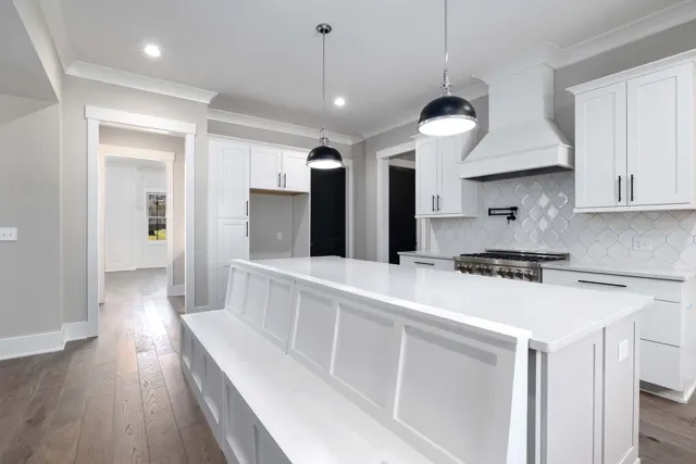 White kitchen cabinets and island beneath dark pendant lights