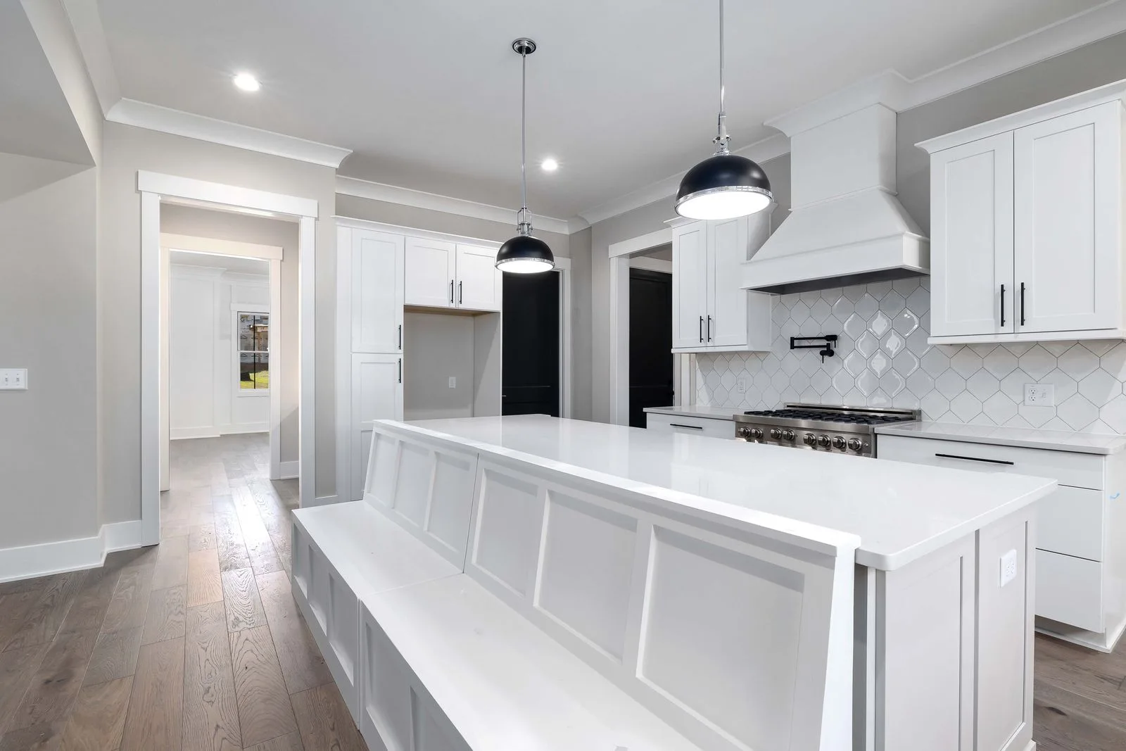 Bright white kitchen with painted cabinetry, a large island, and dark pendant lights